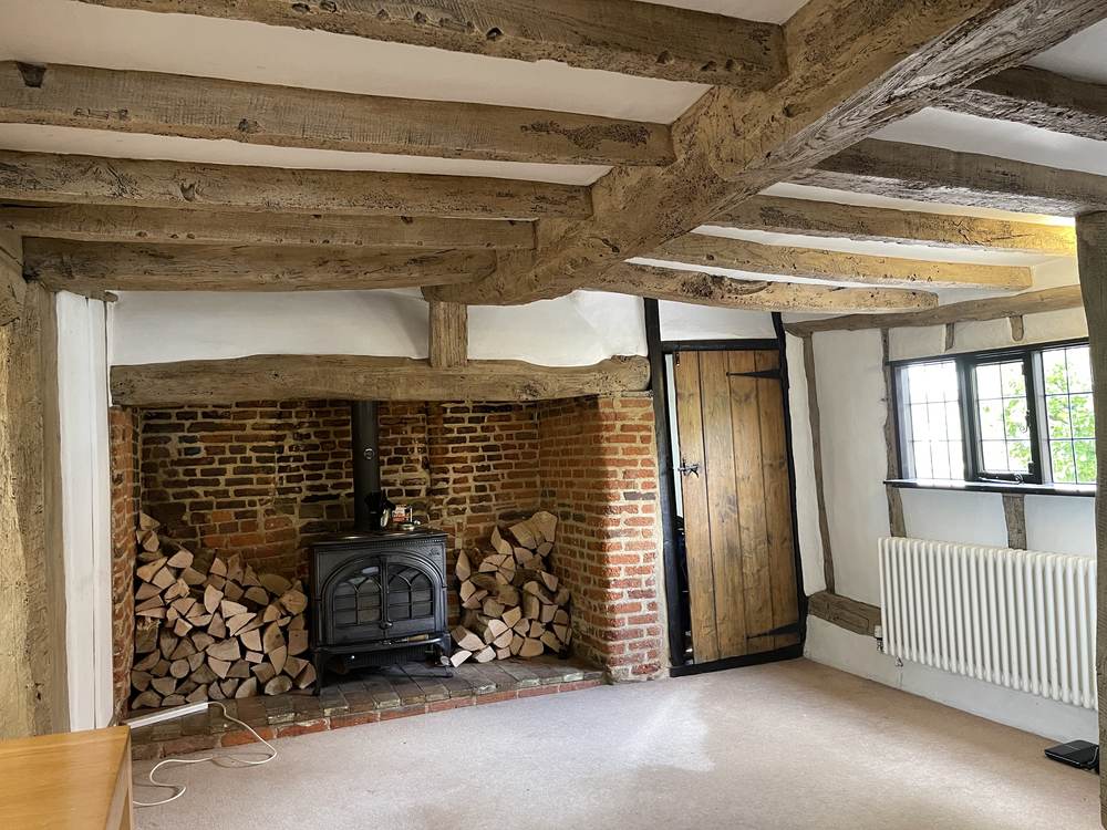 Beamed sitting room with inglenook fireplace and wood-burning stove after restoration
